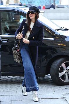 a woman is walking down the street with her hand in her pocket and wearing high heels