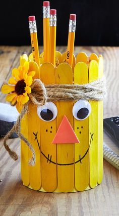 a pencil holder made out of pops sticks with a scarecrow face and sunflower on top