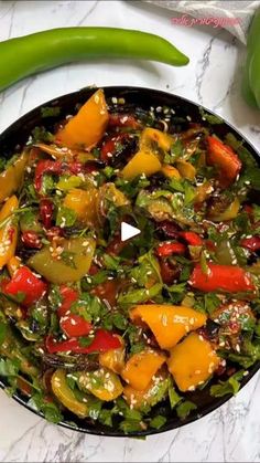 a skillet filled with vegetables on top of a white counter next to green peppers