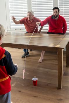 two men and a young boy playing with a string on a table in the living room