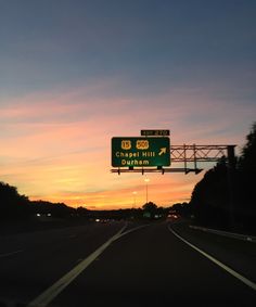 a highway sign on the side of a road at sunset with trees in the background