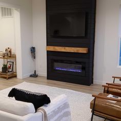 a living room with white furniture and a large tv mounted on the wall above an electric fireplace