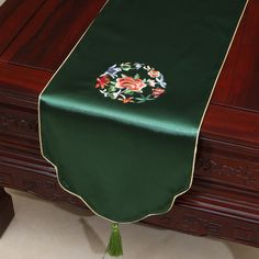 a green table runner with flowers on it and a tassel hanging from the edge