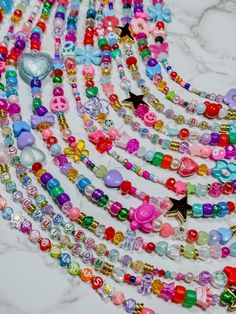 multicolored necklaces are arranged on a marble surface with a heart shaped brooch