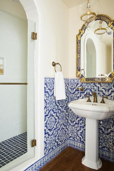 Mediterranean bathroom design boasts blue Moroccan style wall tiles surrounding a pedestal sink fitted with a dark brass faucet under an ornate blue and gold mirror. Greek Style Bathroom Blue And White, Gold Mirror Bathroom Ideas, Blue Moroccan Tiles Bathroom, Amalfi Bathroom Ideas, Portuguese Style Bathroom, Andalusian Bathroom, Medditeranean Tile, Italy Theme Bathroom, Bathroom Ideas Mediterranean