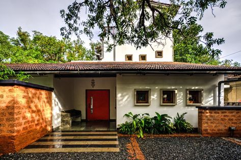 Navovado is a luxury vacation house located in Goa's countryside. The front facade has a low pitched tiled roof that merges with the scale of the neighbouring homes. At the same time, the facade is contemporary with clean lines, a red door and a composition of square pre-cast windows in exposed concrete. Goan Homes, Earthy Luxury, Sandstone Cladding, Kerala Traditional House, Front Facade, Kerala House, John Thomas, Exposed Concrete, Natural Building