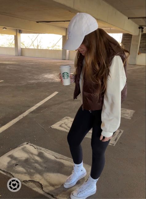 Girl in white baseball hat looking down at feet in parking garage. She is wearing white converse with black leggings, light yellow sweatshirt with brown cropped vest. Vest And Hat Outfits, Baseball Mom Outfits Casual, Outfits With Brown Vest, White Cap Outfits For Women, White Nike Hat Outfit, Brown Cropped Vest Outfit, Baseball Mom Outfits Cold, Beige Baseball Hat Outfit, Brown Baseball Cap Outfit