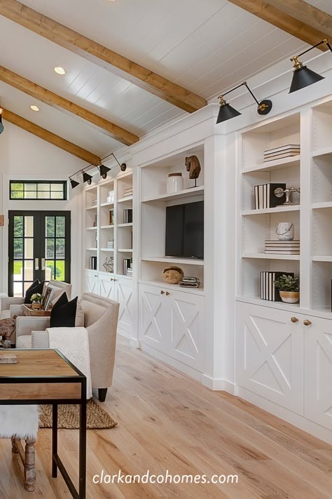 White oak flooring and ceiling beams, with white built-ins and accented by black light fixtures all contribute to the look of this Modern Farmhouse great room. #greatroom #modernfarmhouse #woodflooring #ceilingbeams #builtins #shiplapceiling Built Ins With Ceiling Beams, Built In With Lights, Built In Bookcase Lighting, Floor To Ceiling Entertainment Center, Floor To Ceiling Built Ins, Built Ins With Sconces, Modern Farmhouse Built Ins Living Rooms, Greatroom Builtins, Floor To Ceiling Cabinets Living Room