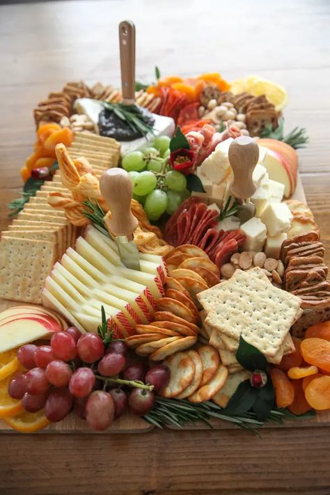 Looking for something to bring to a party? This Thanksgiving Charcuterie Board how-to has everything you need to create a professional cheese board in your home for just $60! With ingredients from Trader Joe's and a step-by-step assembly, you can have a professional cheese board presentation in time for your girls night appetizer spread or Thanksgiving dinner appetizers in no time. Start with cheese and meats, add fruit, layer in crackers, fill in gaps with nuts, and decorate with herbs and ... Cheese And Snack Board, Best Trader Joes Charcuterie, Lunch Charcuterie Boards, Cheese And Cracker Charcuterie Board Ideas, Wine Tasting Cheese Board, Decorate Charcuterie Board, Cheese Presentation Ideas, Cheese Board Trader Joes, Thanksgiving Charcuterie Board Trader Joes