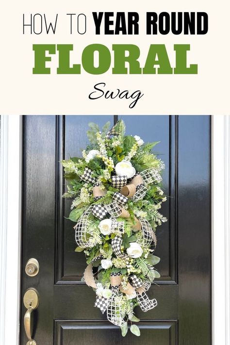 Tear drop shaped floral arrangement hanging on a black front door. Made of tons of faux greenery some leaf like and others and evergreen pine needle look.Think white flowers, tiny white flowers and white roses all placed around one large bow made of black and white check pattern, and white mesh ribbon and a brown ribbon with a black edge and white polka dots. Teardrop Swag Wreath, Making A Swag Wreath, How To Make A Teardrop Swag, Teardrop Swag Diy, Spring Door Swag, Teardrop Wreaths For Front Door, Diy Teardrop Wreath, Flower Swags Diy, How To Make A Swag Wreath