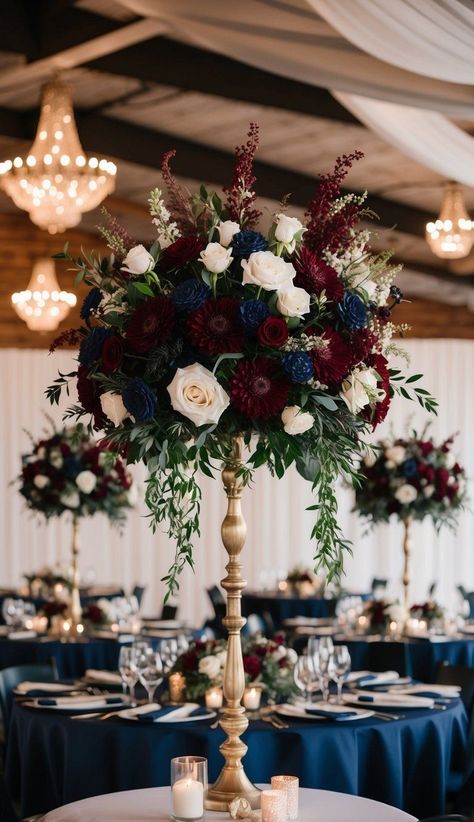 I recommend combining burgundy and navy flowers for stunning wedding centerpieces. Deep red roses, dahlias, or peonies create a rich contrast against navy blue delphinium or hydrangeas. Maroon Blue And Gold Wedding, Navy Blue Flowers Wedding, Red White Blue Gold Wedding, Burgundy Pink And Blue Wedding, Burgundy Blue And Gold Wedding, Navy And Red Wedding Decor, Burgundy And White Flower Arrangements, Navy Blue Burgundy Champagne Wedding, Navy Blue Burgundy Gold Wedding Decor