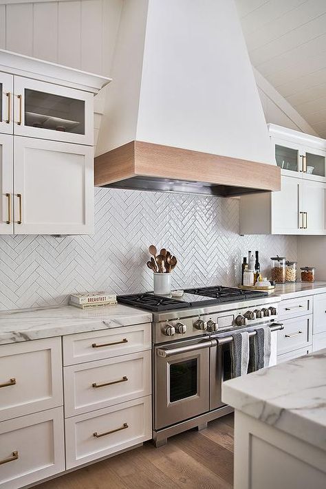 Kichen features a wood trimmed range hood with white herringbone backsplash tiles and marble topped white cabinetry with brass pulls. Herringbone Tiles Kitchen, Herringbone Kitchen Backsplash, White Herringbone Backsplash, Marble Top Kitchen Island, White Herringbone Tile, Herringbone Tile Backsplash, Herringbone Kitchen, Blue Laundry Rooms, Shiplap Backsplash