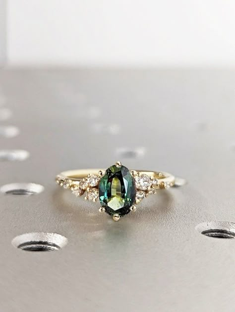 Blue Green Sapphire Ring. Peacock Engagement Ring. Oval Teal Sapphire Ring. 14K Yellow Gold Engagement Ring. Cluster Diamond Ring. Art Deco. * Images show 14K Yellow Gold option. This exquisite peacock sapphire features a stunning oval cut with blue-green hues. Set in a delicate six-prong arrangement, the ring boasts a unique snowdrift cluster adorned with shimmering moissanites or diamonds, creating a captivating and distinctive piece. MAIN STONE Type: Natural Sapphire Cut: Oval Total Carat Est Sapphir Engagement Ring, Types Of Diamonds Colors, Green Sapphire Engagement Ring Oval, Engagement Rings Gold Sapphire, Engagement Ring Green Sapphire, Green Sapphire Engagement Ring Gold, Green Sapphire Engagement Rings, Gem Stone Engagement Rings Vintage, Non Traditional Wedding Rings Engagement