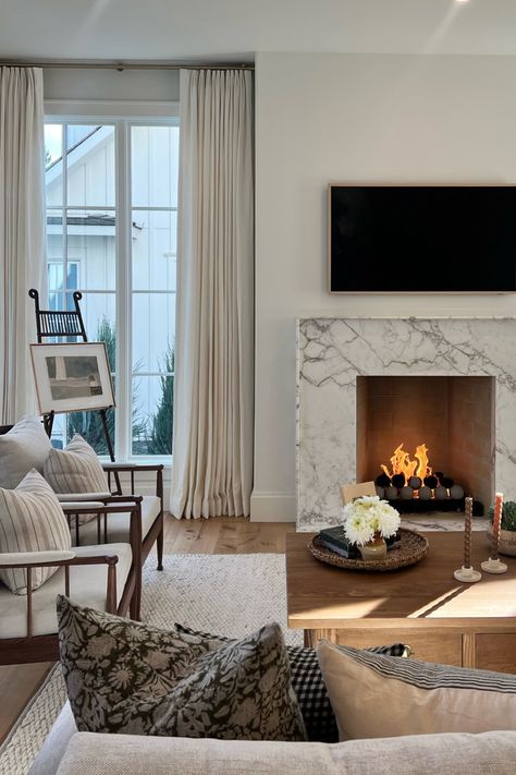 I can't get over the details in this English Cottage inspired living room nestled in the heart of Edina, MN! The creamy white walls allow the stunning marble fireplace surround to shine! The gorgeous over-sized windows allow tons of light in this ultra-cozy space!   New Construction | Home Trends 2024 | Home Design | Minnesota Home Trends Windows Both Sides Of Fireplace, Fireplace With Window On One Side Only, Small Windows Beside Fireplace, Fireplace With Small Windows On Sides, Electric Fireplace With Windows On Each Side, Windows Flanking Fireplace, Fireplace With Windows On Both Sides, Fireplace Windows On Each Side, Windows Next To Fireplace