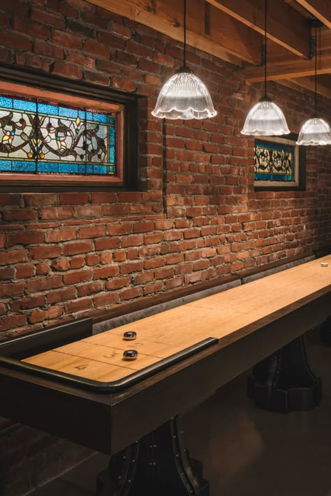 Shuffleboard! A basement converted into a 1920's speakeasy-style man cave. Design features include reclaimed brick, antique stained glass windows, scalloped pendant lighting and concrete flooring. Designed by Fabian Genovesi and built by Neil Kelly Company in Portland, Oregon. Adu Decor, Basement Speakeasy, Bar Lounge Room, Speakeasy Decor, 1920s Speakeasy, Daylight Basement, Antique Stained Glass Windows, Whiskey Room, Cave Basement