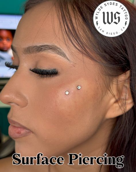 Surface piercings are different from dermal implants - they are a single piercing using a surface bar. All jewelry used is hypoallergenic implant-grade titanium for sensitive skin. For piercing prices, check out our website at www.wyldesydestattoo.com or call 619-575-6792 #bodypiercing #piercing #surfacepiercing #wyldesydestattoo #sandiego #piercingstudio Surface Cheek Piercing, Chin Piercing Women, Surface Piercing Face, Dermal Face Piercing, Dermal Piercing Face, Anti Eyebrow Piercing, Chin Piercing, Face Dermal, Dermal Implants