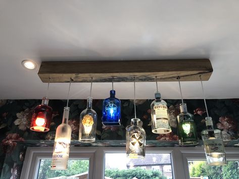 Repurposed alcohol bottles with the bottoms removed. Then turned into pendant lights suspended from an oak beam. Alcohol Bottles Decoration Ideas, Gin Bottles Upcycle, Bottle Ceiling Lights, Liquor Bottle Light Fixtures, Whisky Bottle Lights, Gin Bottle Lights, Gin Bottle Lamp Diy, Whisky Bottle Chandelier, Liquor Bottle Lights