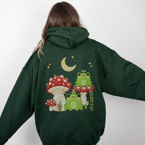 PLEASE NOTE:  This is an adult UNISEX hoodie. Check the Size and Color charts in the listing's photos before placing your order. This kawaii cottagecore mushroom frog hoodie will look very whimsical on you!  Makes for a great gardening gift as well.  There are no side seams. A kangaroo pocket hangs in front. The hood's drawstring is the same color as the base sweater.  ◐ 50% cotton, 50% polyester ◐ Medium-heavy fabric (8.0 oz/yd² (271 g/m ◐ Classic fit ◐ Tear-away label ◐ Runs true to size Frog And Mushroom, Frog Hoodie, Mushroom Frog, Kawaii Hoodie, Cottagecore Mushroom, Cottagecore Clothes, Hoodie Cute, Anime Hoodie, Cute Frogs