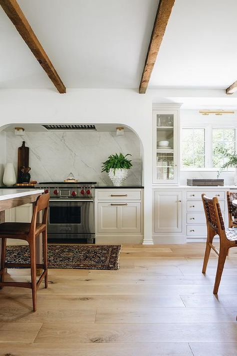 A curved stone cooking alcove is fitted with a Wolf range placed between light gray kitchen cabinets adorned with aged brass hardware and contrasted with a black countertop. Stove Alcove, Kitchen Trends 2021, Alcove Ideas, Jean Stoffer Design, Tudor Kitchen, Jean Stoffer, Top Kitchen Trends, Family Room Remodel, Tudor Style Homes