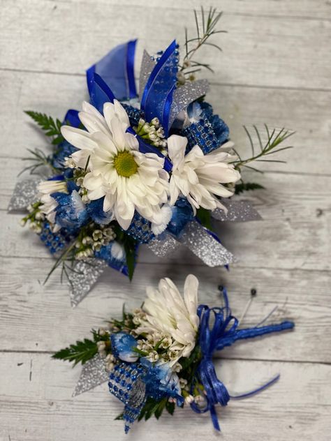 White daisies, tinted royal blue mini carnations with royal blue glitter sprinkled on them.  We used wax flower for fill and royal blue and silver ribbon. Royal Blue Hoco Corsage, Royal Blue And Silver Corsage, Royal Blue Homecoming Flowers, Royal Blue Corsage And Boutonniere Prom, Royal Blue And White Corsage, Blue And Silver Corsage, Royal Blue Corsage And Boutonniere, Blue And White Corsage, Royal Blue Corsage