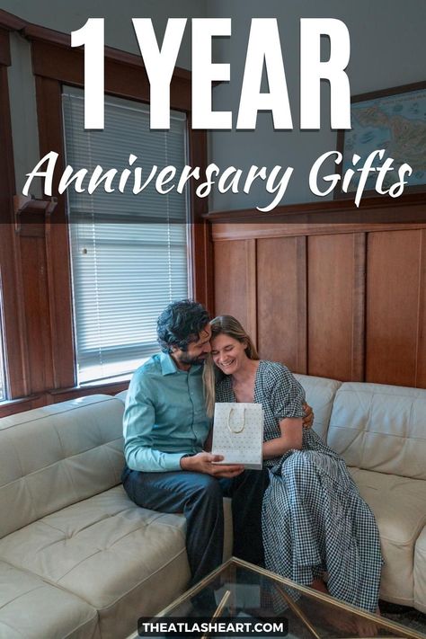 A man in a blue shirt embraces a woman in a gingham maxi dress and hands her a white gift bag as they sit in the corner of an L-shaped, white leather couch, with a wood-paneled interior in the background and the text overlay, "1 Year Anniversary Gifts." Gift Ideas For One Year Anniversary, First Anniversary Ideas For Husband, 1year Anniversary Ideas, First Anniversary Ideas, Paper Gifts For Him, First Anniversary Gift For Husband, One Year Gift, Gifts For Husbands, Anniversary Journal