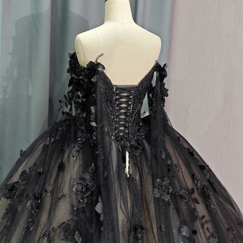 Timeless vintage-inspired Black Sweetheart Quinceanera Dress. Featuring an intricate beadwork bodice, off-the-shoulder long sleeves with a dramatic floral drape shoulder cape, this dress exudes glamour and luxury. The black lace overlay complete with hand sewn florals adds a touch of elegance, while the adjustable lace-up back ensures a perfect fit. Elevate your party look with this exquisite ball gown. material: glitter tulle, organza type: ball gown style: formals color as shown built in bra sweetheart neckline train as shown lace up back Black Dress Fairytale, Emo Ball Gown, Black Quince Dresses With Sleeves, Black Gowns Dresses Elegant, Black Quinceanera Dresses With Gold, Black And Silver Quinceanera Dresses, Black And White Quinceanera Dresses, Emo Quinceanera, Black Ball Gown Elegant