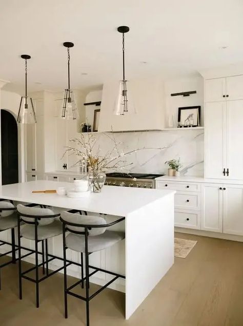 a beautiful modern kitchen with white shaker cabinets, a white quartz backsplash, a white kitchen island and glass pendant lamps White Quartz Waterfall Island, Quartz Backsplash Kitchen Window, Clear Kitchen Island Pendants, Small White Kitchen Pendant Lights, Quartz Countertop And Backsplash, Quartz Countertops With White Cabinets, White Quartz Countertop Kitchen, Quartz Backsplash Kitchen, Granny Cottage