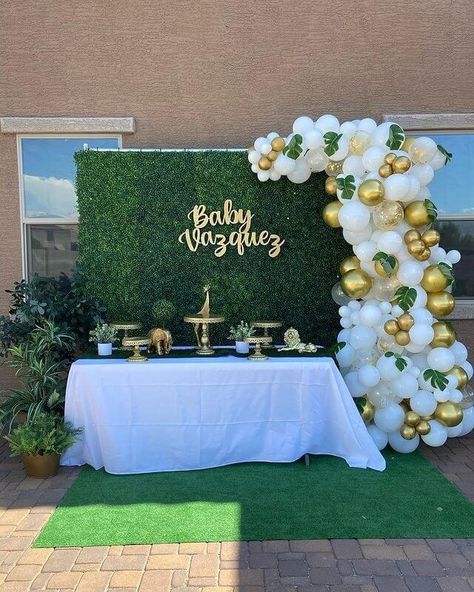 Welcome your baby with a garden inspired outdoor table setup to elevate your baby shower party décor. Use a white tablecloth for your tabletop and arrange gold cake and cupcake stands over it to place your sweet confectioneries. Maximize its beauty by using faux plants that match your green table runner. Opt for an artificial grass wall for your backdrop adorning it with uniquely set white and gold balloons. Add finishing touches with some large sized fake plants that’ll exude refreshing vibes. Green And White Decorations Party, Expo Backdrop, White And Gold Balloons, Garden Party Decorations Diy, Greenery Party, Cake Table Backdrop, Event Decor Ideas, Party Decorations Table, Balloons Cake