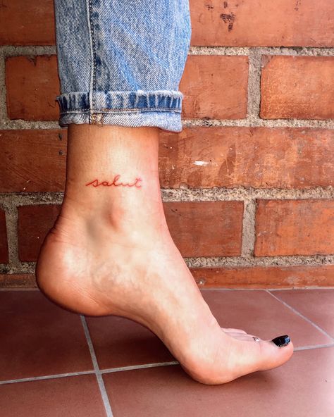 Tattoo word in red ink on ankle Ankle Tattoo With Words, Outside Of Ankle Tattoo, Above The Ankle Tattoo, Word Tattoo On Ankle, Ankle Tattoos For Women Words, Name Tattoo On Ankle, Red Foot Tattoos, Ankle Tattoo Small Words, Ankle Script Tattoo