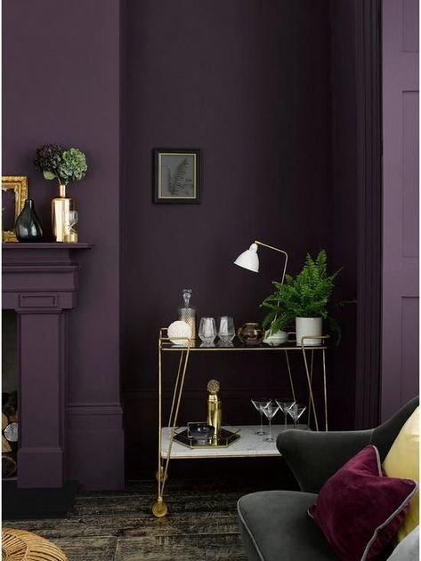 a moody living room with an aubergine accent wall, a fireplace, a delicate gold bar cart and a black sofa with colorful pillows Deep Purple Wall Color, Deep Purple Room Ideas, Deep Purple Walls, Dark Purple Wall Paint, Purple Walls Living Room, Eggplant Paint Color, Plum Living Room, Dark Purple Bedroom, Dark Purple Wall