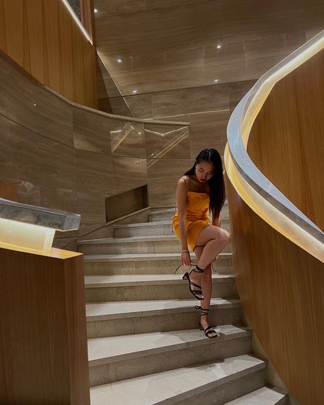 Young woman wear orange summer dress styled with black strappy block heels standing in a staircase in hotel lobby Poses In Heels And Dress, Poses On Stairs Instagram Dress, Tying Shoes Pose, Stairs Poses Instagram, Pictures On The Stairs, Poses With Heels, Orange Heels Outfit, Staircase Poses, Stairs Poses