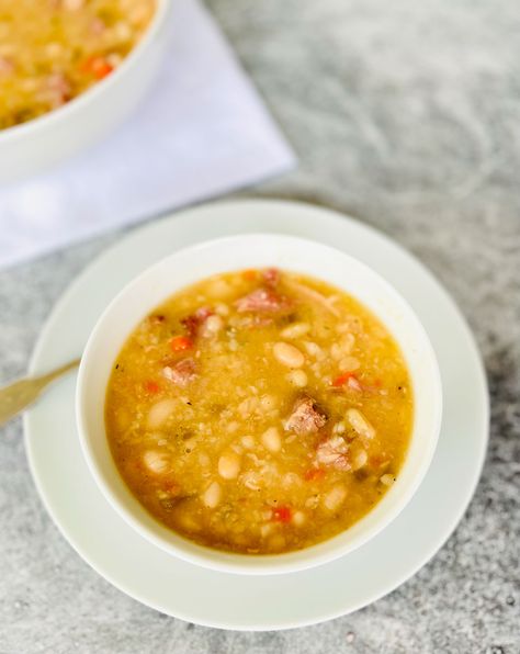 Small white round bowl with bean soup in it. Bowl is on a white round plate. There is a silver spoon resting on the plate. There is a large white round bowl with bean soup in it in the background. Bowls are on a light gray surface. Senate Bean Soup Recipe, Senate Bean Soup, Navy Bean Soup, Simple Soup, Bean Soup Recipe, Soup Beans, Ham Bone, Bean Soup Recipes, One Pot Meal