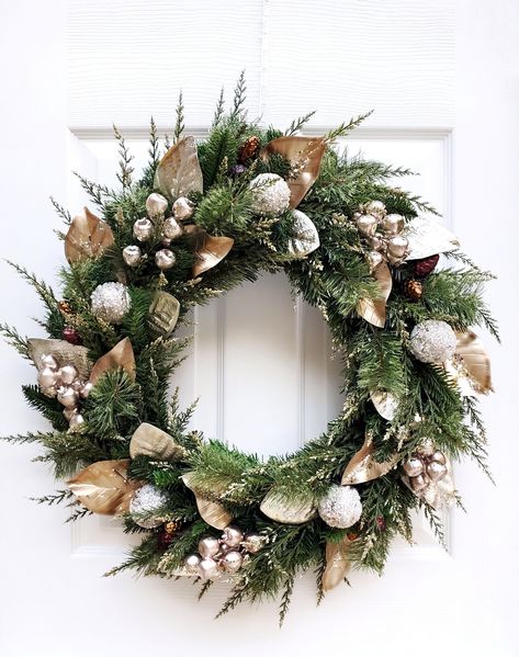 "This beautiful champagne and gold magnolia winter wreath is the perfect way to welcome guests into your home during the holiday season. It may also be used as a lovely accent for a winter wedding. This wreath includes champagne and gold magnolia leaves, large champagne gold berry clusters, gold tipped cedar, icy gold glitter ornaments, and pinecone ornaments nested in a pine wreath base form. Due to shipping, this item measures approximately 20\" in diameter and may need some slight \"fluffing\ Christmas Wreaths For Front Door With Ornaments, Christmas Wreaths Gold And Silver, Silver And Gold Wreath, Champagne Christmas Wreath, Silver And Gold Christmas Wreath, Gold Christmas Wreath For Front Door, Christmas Decor White And Gold, Black And Gold Christmas Wreath, White And Gold Wreath