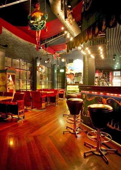 Vibrant, oppulent circus themed room adorned with bright stage lights and red embelishments with trapeze artist on a swing Circus Themed Restaurant, Circus Restaurant, Circus Interior, Circus Room Aesthetic, Circus Ceiling, Vintage Circus Home Decor, Circus Lighting, Circus Room, Boho Bar