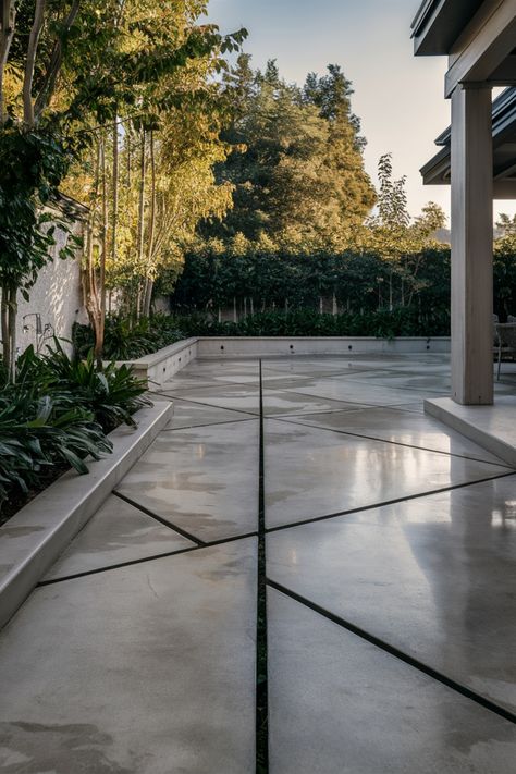 Modern concrete patio with geometric design, surrounded by greenery and shaded by nearby trees. Patio With Concrete Squares, Small Concrete Backyard Ideas, Modern Concrete Patio Ideas, Creative Concrete Ideas, Concrete Backyard Ideas Cement Patio, Concrete Courtyard Ideas, Concrete That Looks Like Pavers, Patio Concrete Ideas, Modern Stone Patio