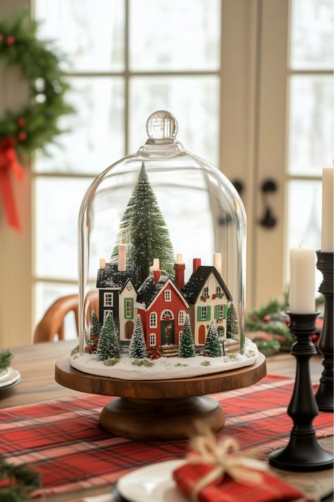 This snowy village Christmas centerpiece feels like stepping into a winter wonderland. Mini houses and trees sprinkled with faux snow sit perfectly under a glass cloche. It’s whimsical, festive, and easy to make—don’t you think it would spark conversations at your holiday gatherings? Glass Tree Centerpiece, Cloche Christmas Ideas, Winter Cloche Ideas, Christmas Village Table Centerpiece, Snowglobe Centerpiece, Christmas Village Centerpiece, Snowy Christmas Decor, Christmas Cloche Ideas, Easy Christmas Centerpieces