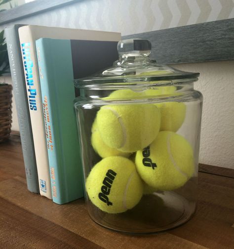 These tennis balls in a glass container are a great way to decorate a sports theme bedroom, and also make for a great book stopper. #Tennis #Decor   Home decor at The Trails at Pine Ave, San Bernardino. Sports Themed Airbnb, Tennis Ideas Crafts, Tennis Bathroom, Tennis Bedroom Ideas, Tennis Ball Cans Ideas, Tennis Office Decor, Sporty Decor, Tennis Nursery, Sports Theme Bedroom