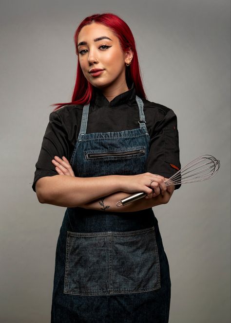 Female pastry chef with bright red coloured hair wearing a black chef jacket and blue denim apron with her arms crossed holding a whisk Chef Studio Photoshoot, Chef Outfit Women Style Classy, Female Chef Photography, Pastry Chef Headshots, Chef Photo Shoot Ideas, Professional Chef Photos, Baker Professional Pictures, Chef Poses Photo Ideas, Chef Headshots Portraits