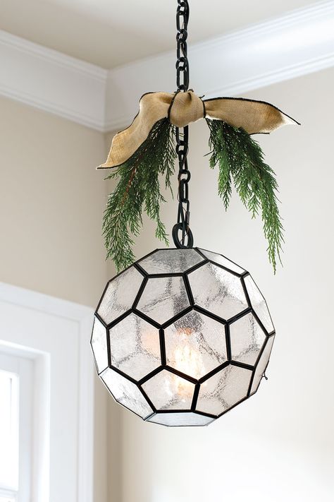 Pendant light with sprigs of greenery and ribbon Greenery On Pendant Lights, Decorate Light Fixture For Christmas, Decorating Light Fixtures For Christmas, Christmas Pendant Light Decor, Christmas Chandelier Ideas, Farmhouse Addition, Christmas Chandelier, Glass Light Fixtures, Christmas Stem