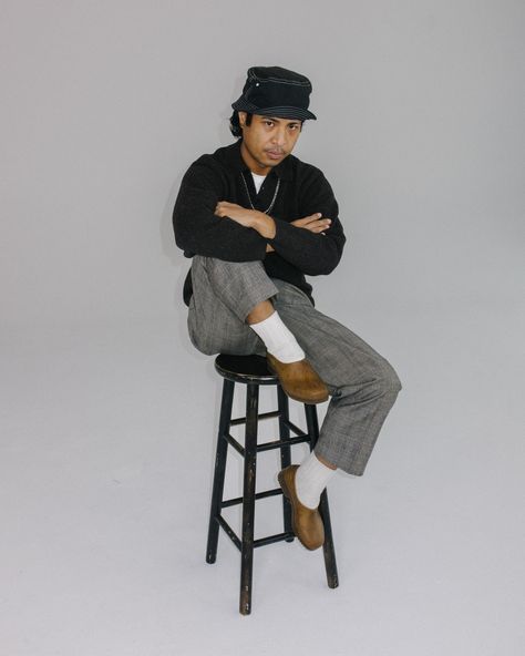 Man wearing bucket hat, white socks, clogs, and gray pants. He is sitting on a stool, arms crossed with one leg up and one leg down. Gardenheir Clogs Outfit, Gardenheir Clogs, Garden Clogs Outfit, Gardana Clog, Clogs Outfit Men, Swedish Clogs Outfit, Styling Clogs, Clog Outfit, Stylish Walking Shoes