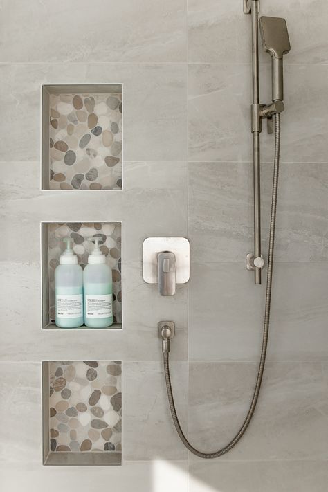 Your shower niche is the perfect opportunity to create some visual interest. Here we used a smooth river stone tile to draw the eye but also to create some material repetition as the tile was also used for the shower floor as well. Design by Kierstin Smyth Design. Photo Credit: Darren Lebeuf #edmontonbathroomrenovation #edmontoninteriordesign #tripleshowerniche Modern Shower Niche Ideas, Shower Inset Shelves, Stone Shower Niche, Small Shower Niche Ideas, Lighted Shower Niche, Washroom Niche Design, Small Ensuite Ideas Narrow, Niche In Shower Wall, Vertical Shower Niche