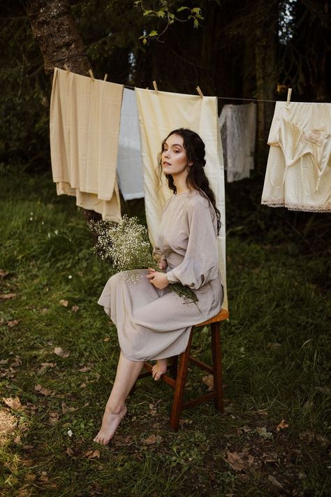 Model is seated on a stool with one foot tucked up and one forward on ground. Model holds a bouquet of baby's breath, and a clothesline with neutral sheets hangs behind her. Laundry Line Photoshoot, August Photoshoot Ideas, Clothes Line Photoshoot, Summer Editorial Photoshoot, Clothing Line Photoshoot Ideas, Clothesline Photoshoot, Laundry Photography, Laundry Photoshoot, Backyard Photoshoot