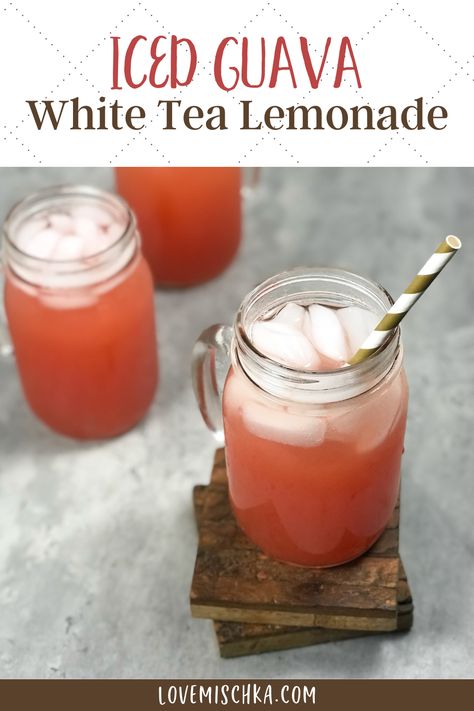 A beautiful, deep reddish pink guava white tea lemonade in a mason jar glass with a handle, full of white ice cubes and with a gold and white striped paper straw in it, sits on two dark brown, wooden coasters, in front of two more tropical pink iced guava white tea lemonades. Guava Starbucks Drink, Guava Drink Recipes, Guava Punch, Fruit Iced Tea Recipes Summer Drinks, Guava Simple Syrup, Tea Lemonade Recipe, Strawberry Guava Lemonade, Lemonade Tea Recipe, Soda Drinks