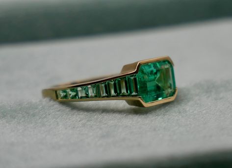 At the centerpiece of this lab grown Colombian emerald ring is a radiant 1.5 ct emerald, set east west to highlight its natural allure. Flanking it are calibre cut emeralds, each uniquely shaped to create a seamless gradient effect, making every ring truly one-of-a-kind. Set in luxurious 18K yellow gold, this ring exudes timeless charm. What makes it truly special? Calibre cut stones are individually shaped to fit precisely into the design, resulting in a mesmerizing display of color and brillia Nonbinary Engagement Ring, Emerald And Sapphire Ring, Emerald Ring Designs, Gold And Emerald Ring, Round Emerald Ring, Gem Cuts, Emerald Green Ring, Emerald Ring Design, Colombian Emerald Ring