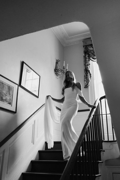 Black and White photo of bride walking down the stairs holding her veil.