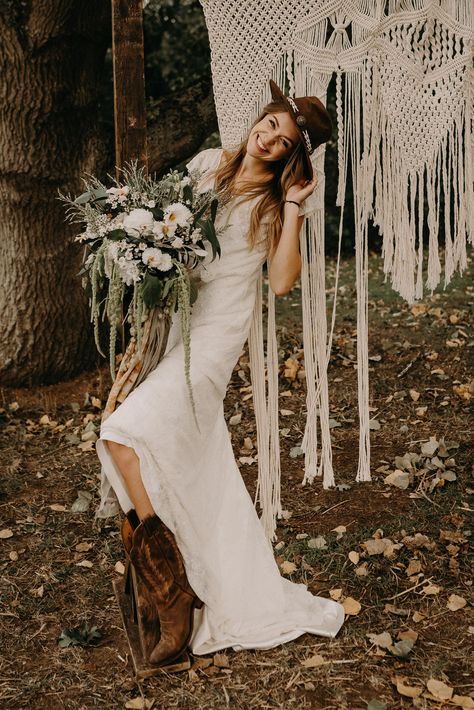 Bride wearing cowgirl boots and hat. Photography by Kelsie Low. Macrame arch for weddings. Bride in wedding dress with oversized wild flower bouquet. Wedding arbour with macrame Hat Macrame, Wedding Cowgirl Boots, Boots Bride, Macrame Dresses, Cowgirl Boots Wedding, Cowgirl Bride, Macrame Arch, Hat Photography, Cowgirl Wedding