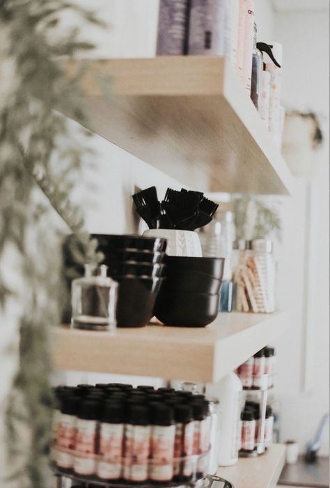 Colorful hair products organized on hanging shelves with plants Hairdresser Organization Ideas, Salon Suite Shelving Ideas, Hairstylist Storage Ideas, Salon Bleach Container, Color Bar Organization, Small Hair Salon Storage Ideas, Salon Color Bar Organization, Salon Hot Tool Storage, Salon Suite Must Haves