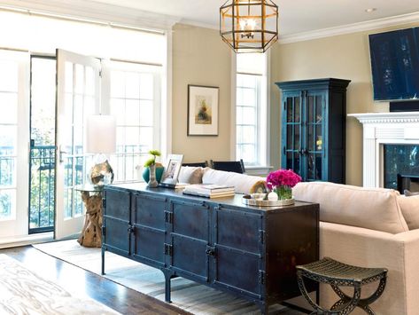 This neutral condo living room features an antique sideboard that serves as a console table behind an off-white sofa. A chandelier with a metal geometric pattern provides light for the space, and a dark glass-front cabinet provides storage and display space. Behind Sofa, Table Behind Couch, Condo Living Room, Behind Couch, Storage Inspiration, Industrial Livingroom, Traditional Interior Design, Transitional Living, Eclectic Living Room