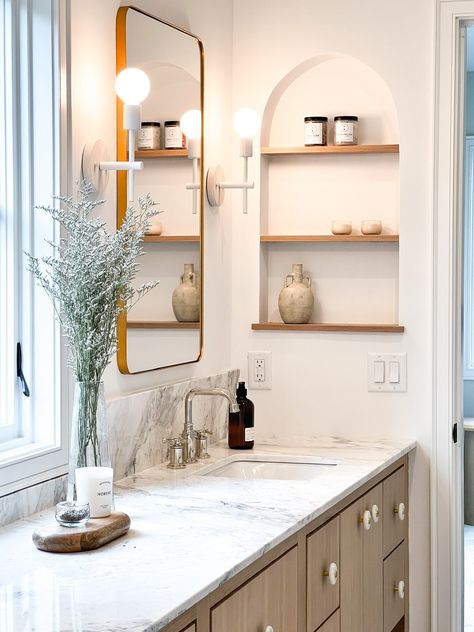 This bathroom has all the most beautiful design features! From the marble countertop and backsplash, the oak vanity and unique knobs, to the arched niche with shelves built into the wall, it truly is impressive!    New Construction | Home Trends 2024 | Home Design | Minnesota Home Trends Arch Niche Bathroom, Built In Niche Bathroom, Arched Niche In Wall Bathroom, Bathroom Vanity Niche, Niche With Shelves, Vanity Niche, Arched Niche In Wall, Niche In Wall, Arched Niche