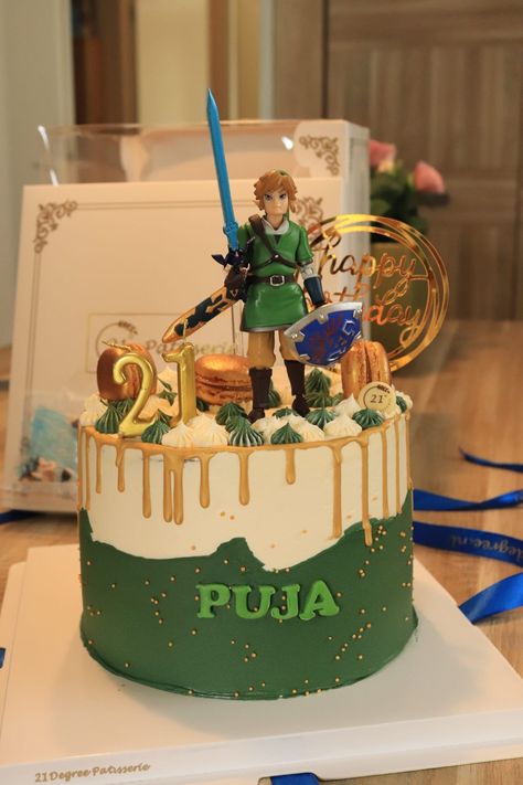 A beautiful birthday cake coloured in green, white, and a dripping gold border, topped with golden macarons and a figurine of Link. Tears Of The Kingdom Cake Ideas, Link Cake Zelda, Zelda Cakes Birthday, Nerdy Birthday Cakes, Zelda Tears Of The Kingdom Cake, Link Birthday Party Zelda, Legend Of Zelda Birthday Cake, Legend Of Zelda Birthday Party Ideas, Zelda Birthday Party Decorations